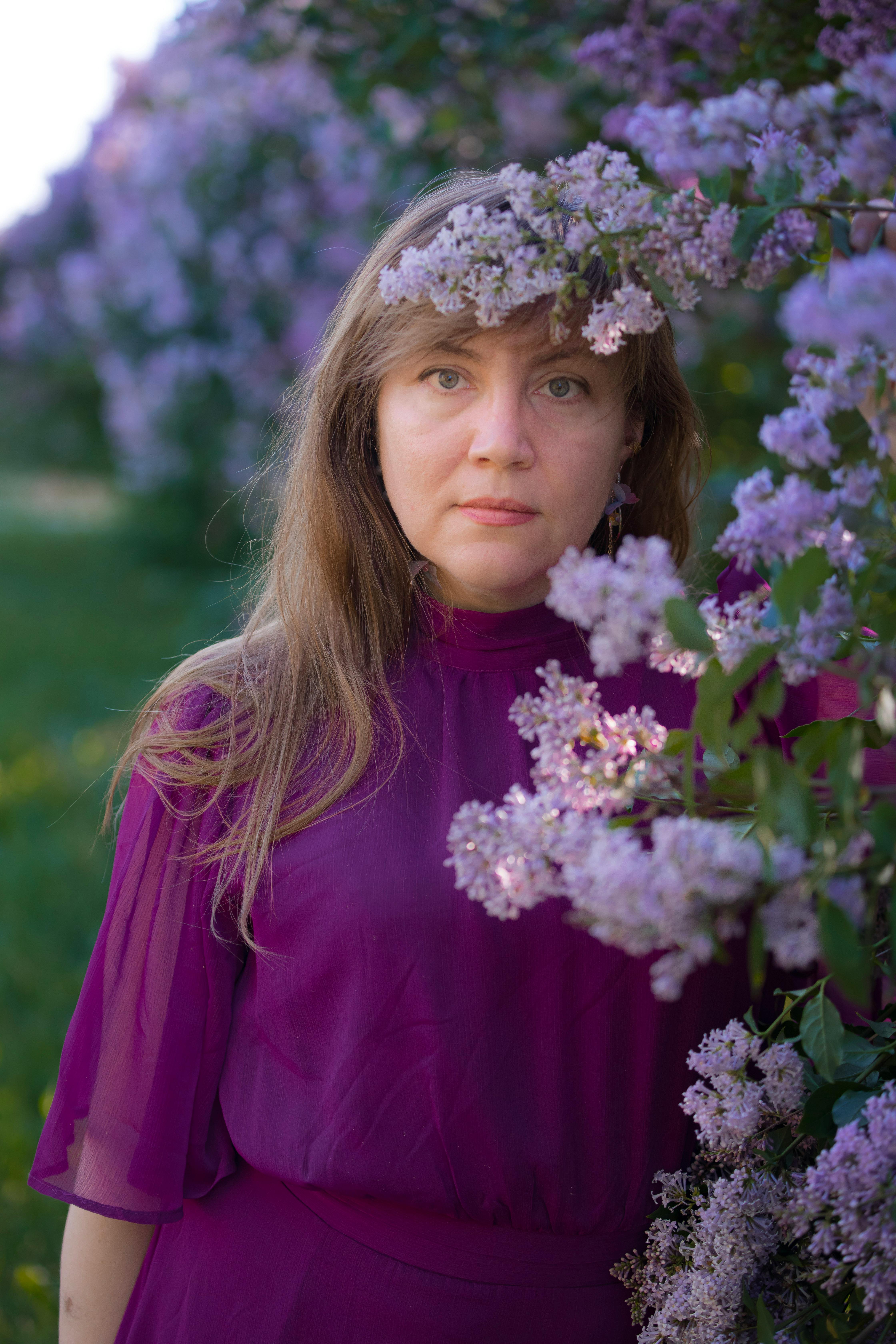 Portrait of a woman in purple attire standing among lilac blossoms in a garden setting during spring.