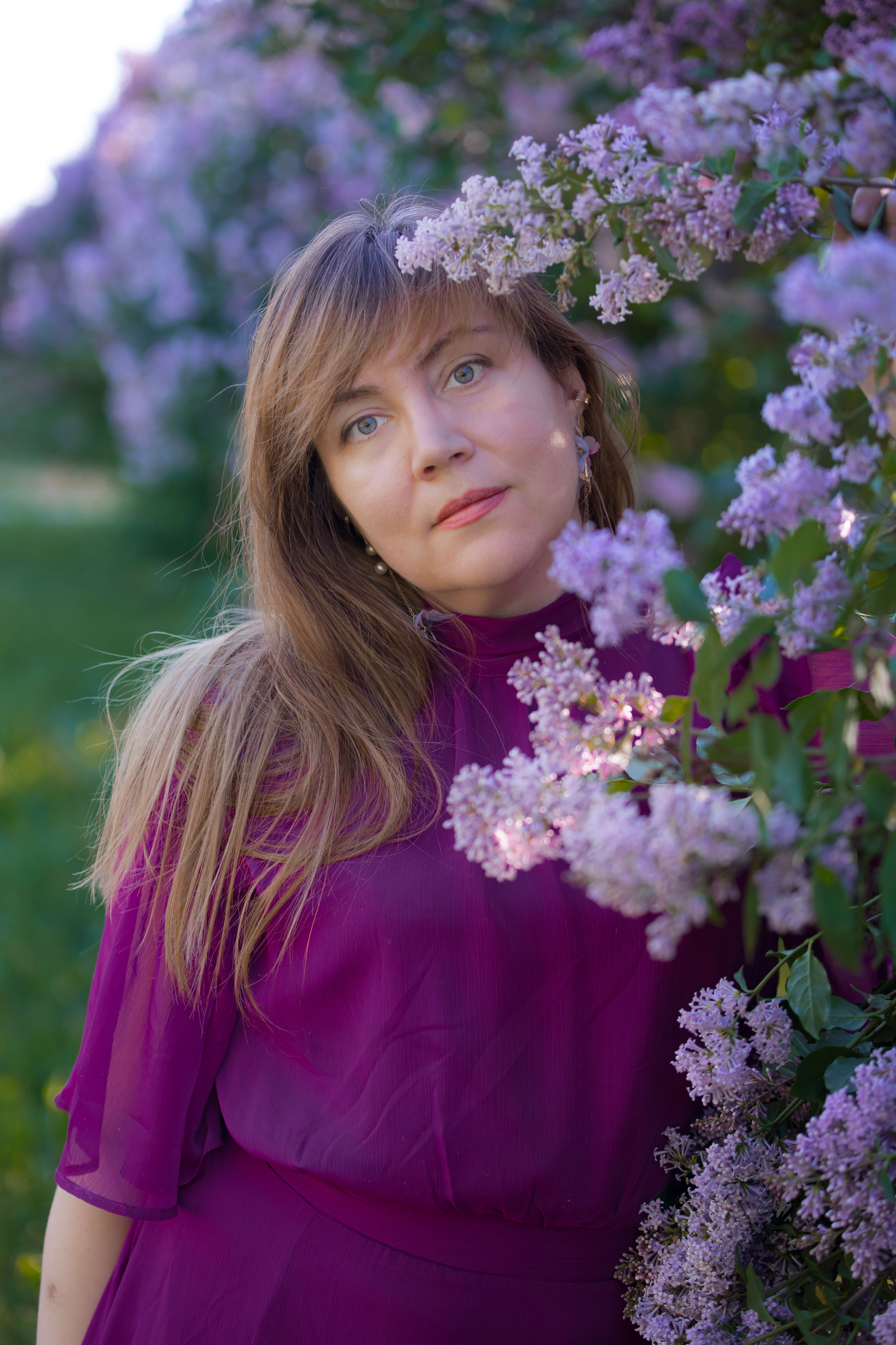 Woman with long brown hair in purple dress among blooming flowers, symbolizing spring.