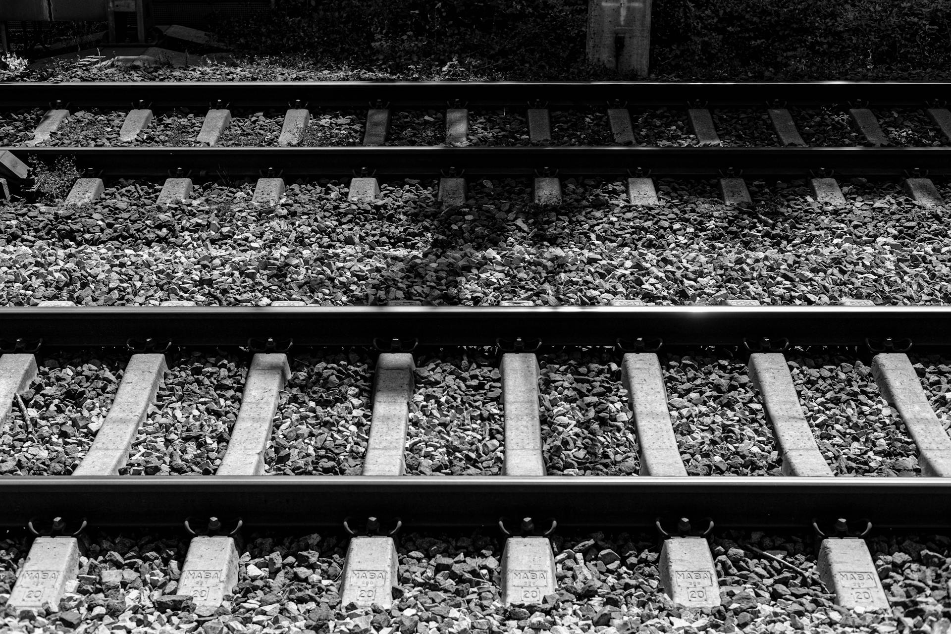 A moody black and white image of railway tracks lined with pebbles and stones.