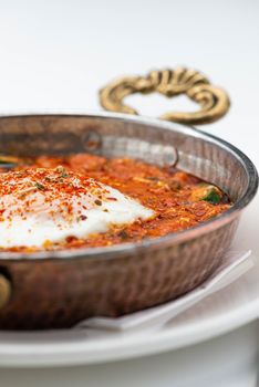 Delicious homemade shakshuka with poached egg, spices in a copper pan.