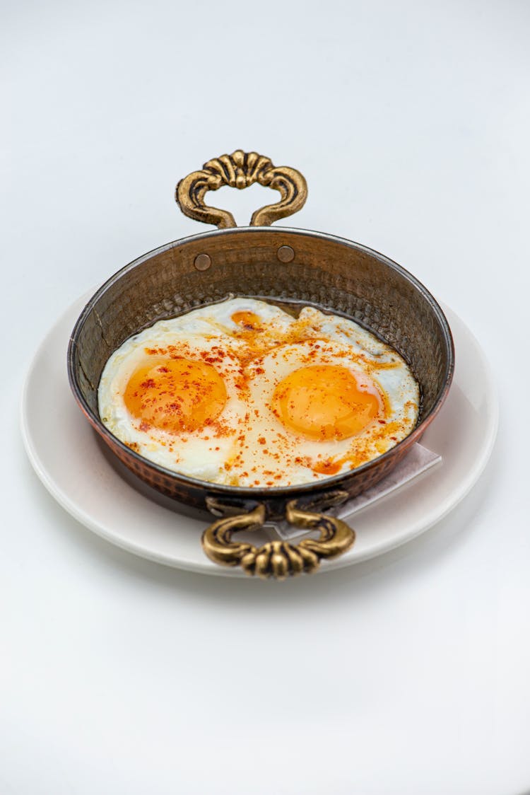 Spiced Poached Eggs On A Brass Saucepan Against White Background