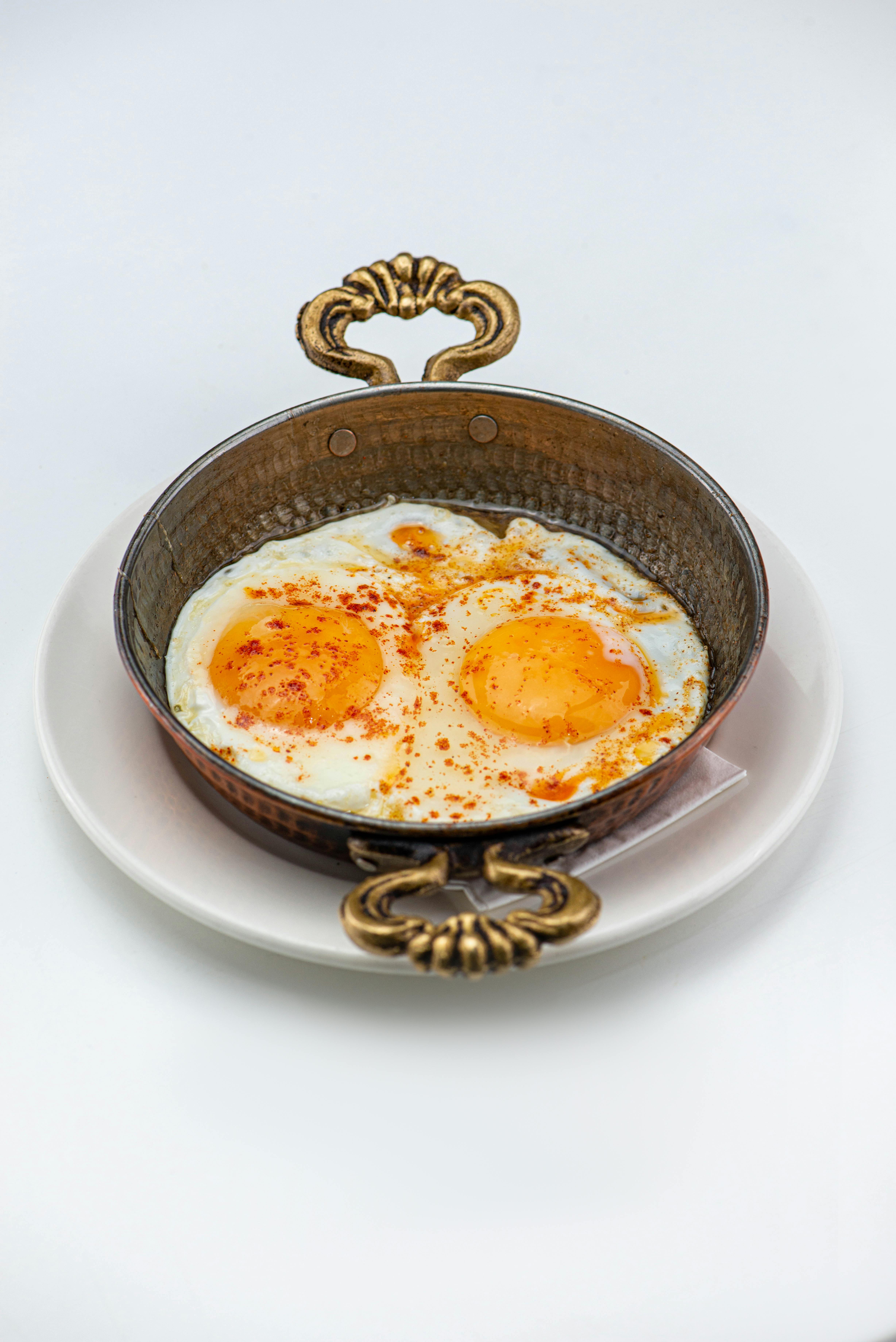 Spiced Poached Eggs on a Brass Saucepan against White Background · Free