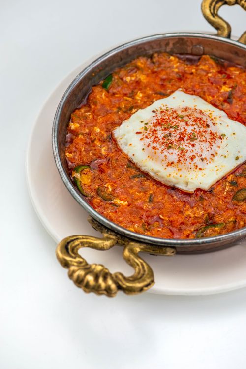 Free Tasty shakshuka dish with poached egg in a copper pan, garnished beautifully, served on a white plate. Stock Photo