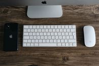 A minimalist workspace featuring a smartphone, keyboard, and mouse on a wooden desk.
