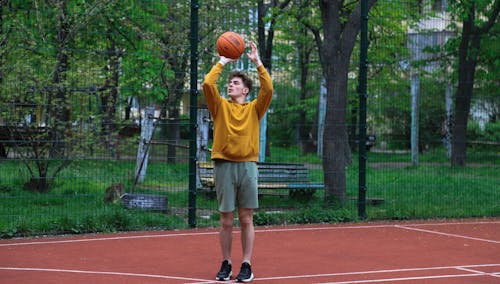 Teenager in Yellow Jumper Throwing Ball on Basketball Court