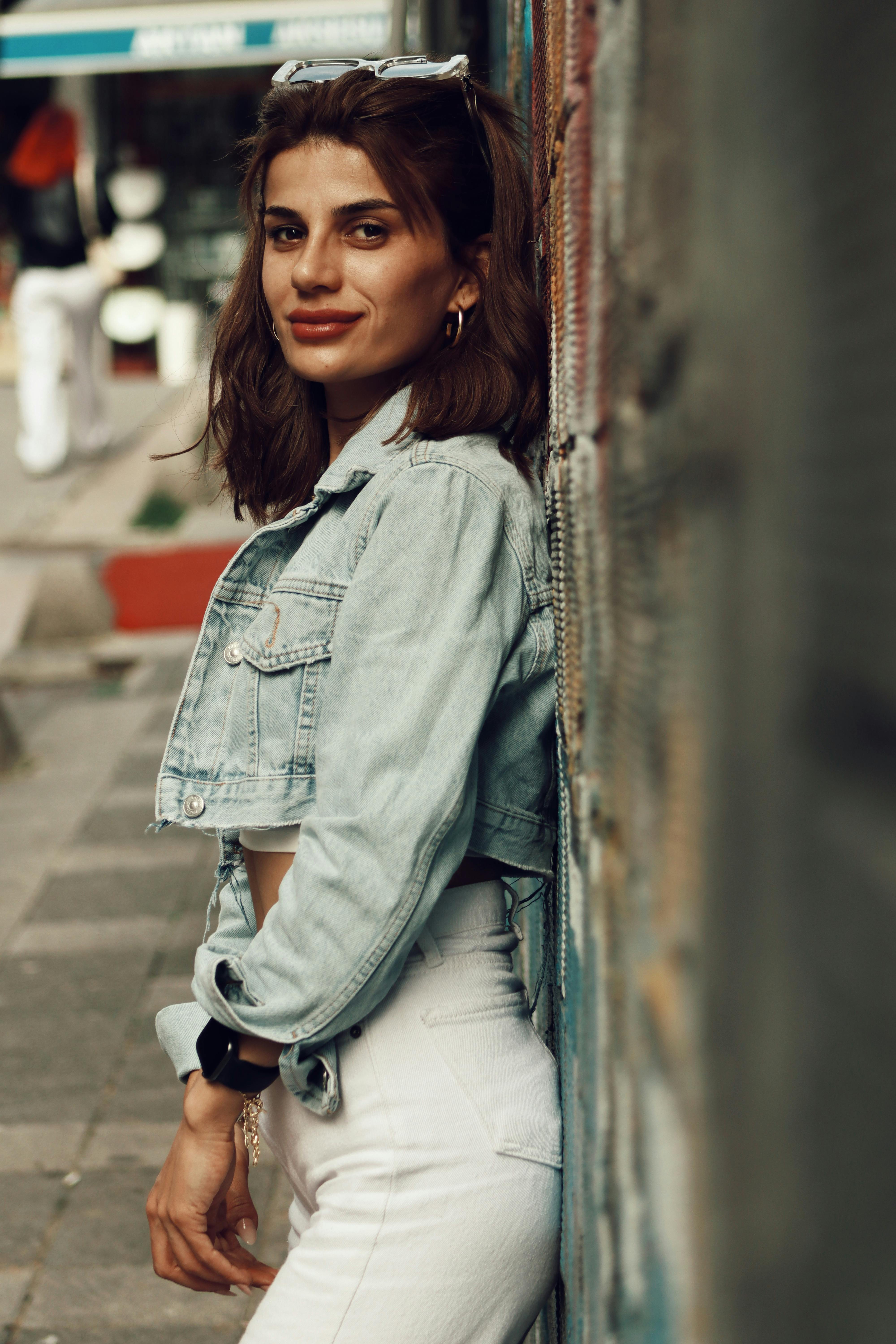 Woman in denim jacket posing against graffiti wall in urban environment.