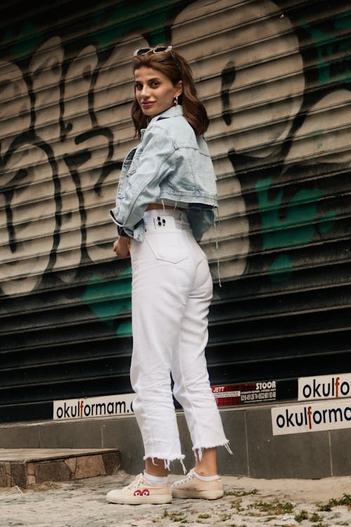 Woman Wearing Jean Jacket and White Pants Standing next to Garage