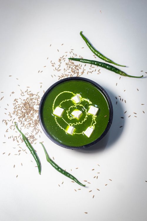 Free Top-down shot of a vibrant green soup with paneer cubes and cumin seeds on a white background. Stock Photo