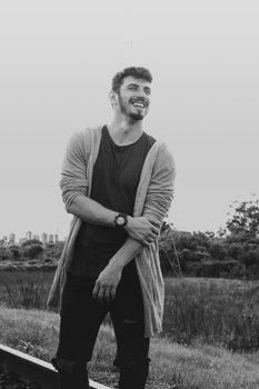 Black and white portrait of a smiling man in casual attire standing outdoors.