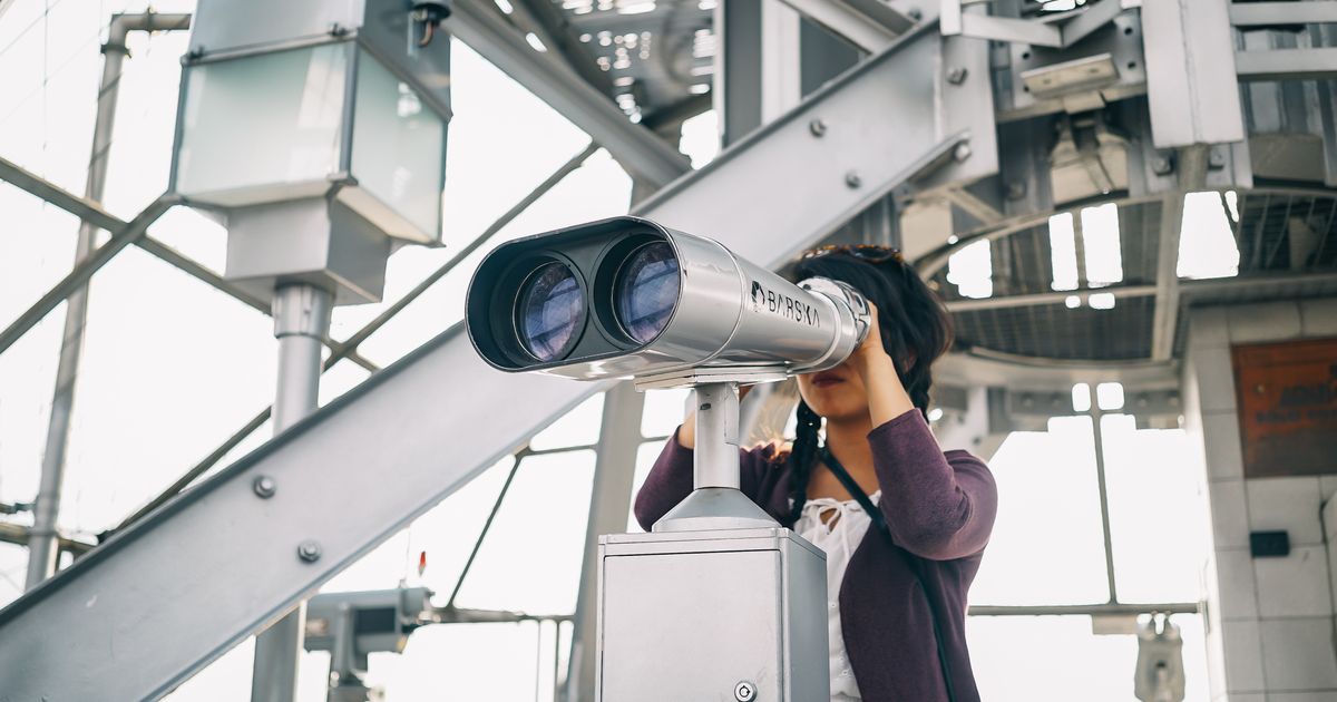 A woman looks through coin-operated binoculars on an outdoor viewing platform