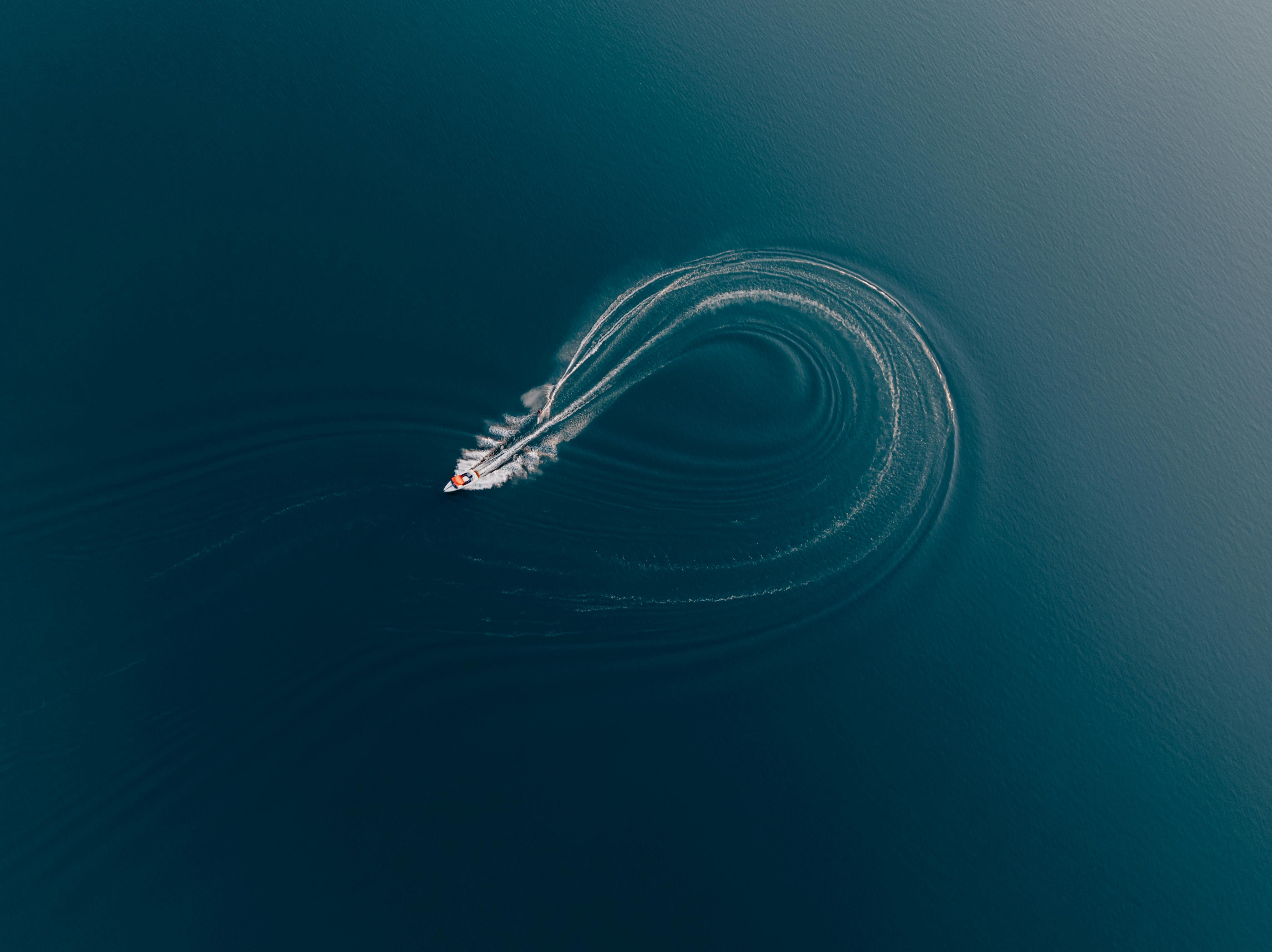 Stunning aerial capture of a motorboat creating spirals in the tranquil blue sea, showing dynamic movement.