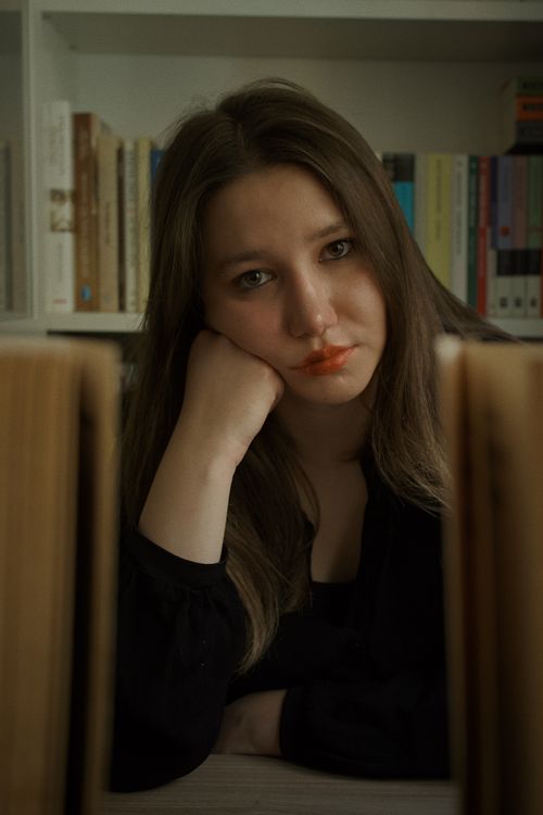 Free A woman sits indoors, thoughtfully leaning on her hand, surrounded by books in a library. Stock Photo