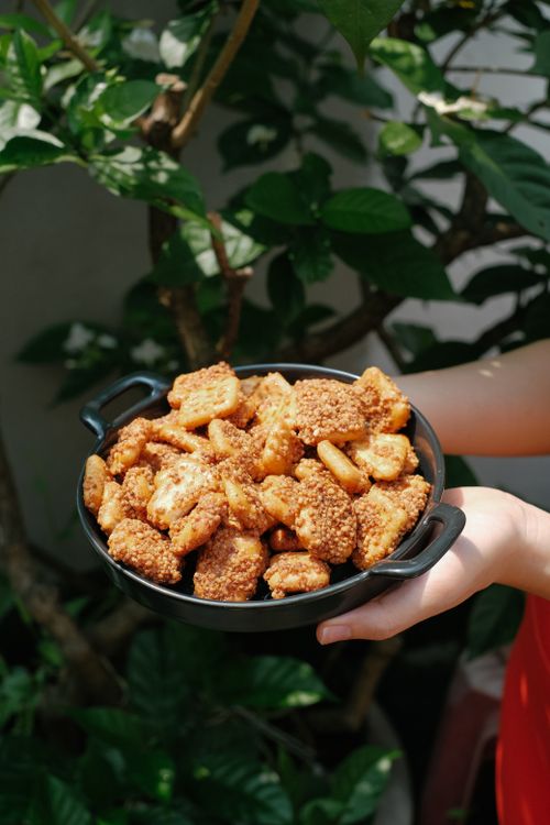 Free Close-up of hands holding a bowl of crispy sesame-coated fried snacks outdoors. Stock Photo