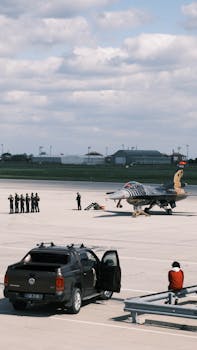 Military jet parked on tarmac with crew and vehicle in İstanbul airport.