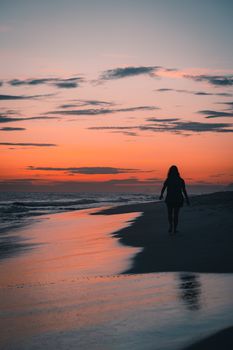 Serene sunset scene with a woman's silhouette walking on a beach in Rio de Janeiro, Brazil.