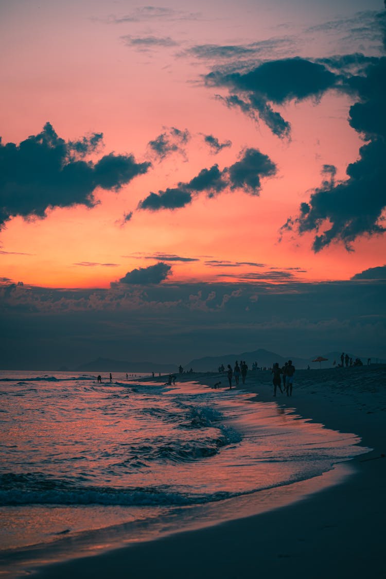 Silhouettes Of People Walking On Seashore On Sunset