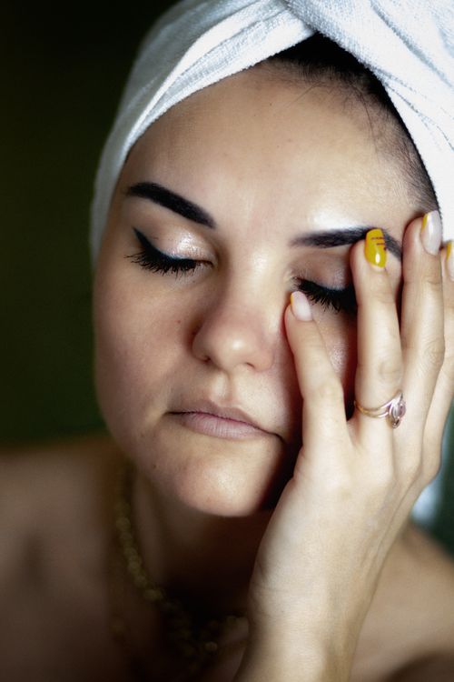 Free Close-up portrait of an adult woman with a towel on her head, applying beauty treatment to her face. Stock Photo