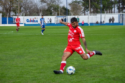 Soccer player in red jersey kicks ball during intense outdoor match.