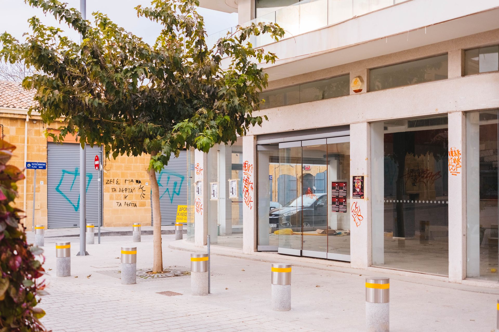 A modern commercial building exterior with glass doors and urban graffiti, street view.