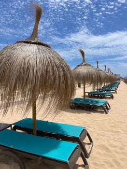Serene tropical beach featuring thatched umbrellas and lined sunbeds on soft sand under a blue sky.