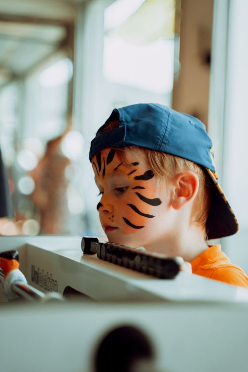 Free Child with tiger face paint wearing a cap, looking down in an indoor setting. Stock Photo
