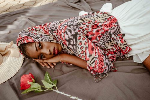 Free Beautiful woman in patterned scarf lying on blanket with rose, exuding elegance and calm. Stock Photo
