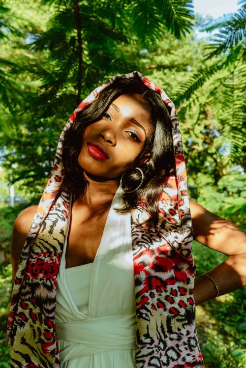 Free Beautiful woman in vibrant scarf enjoying a sunny day in a lush garden setting. Stock Photo