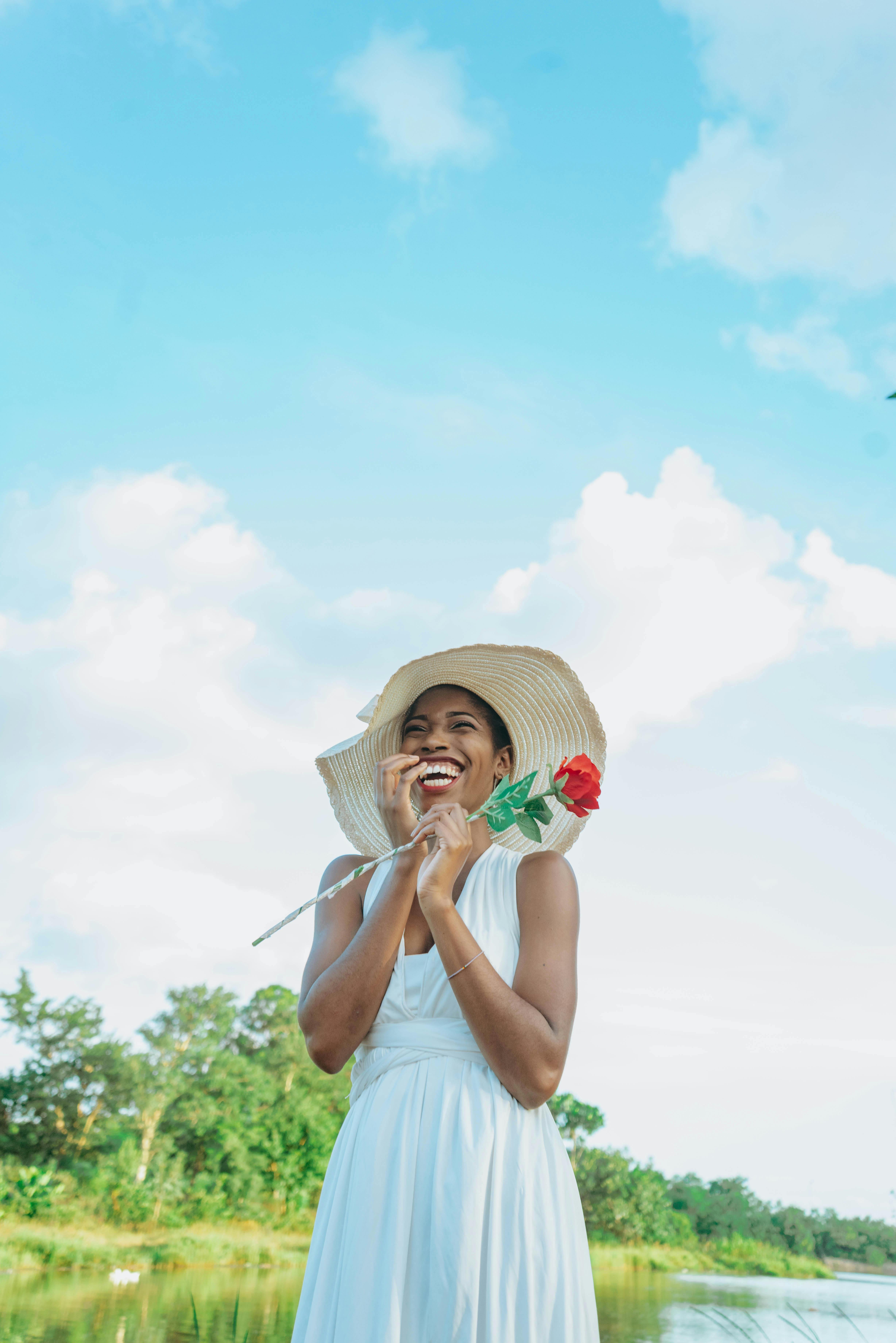 a woman in a white dress and hat is standing by the water