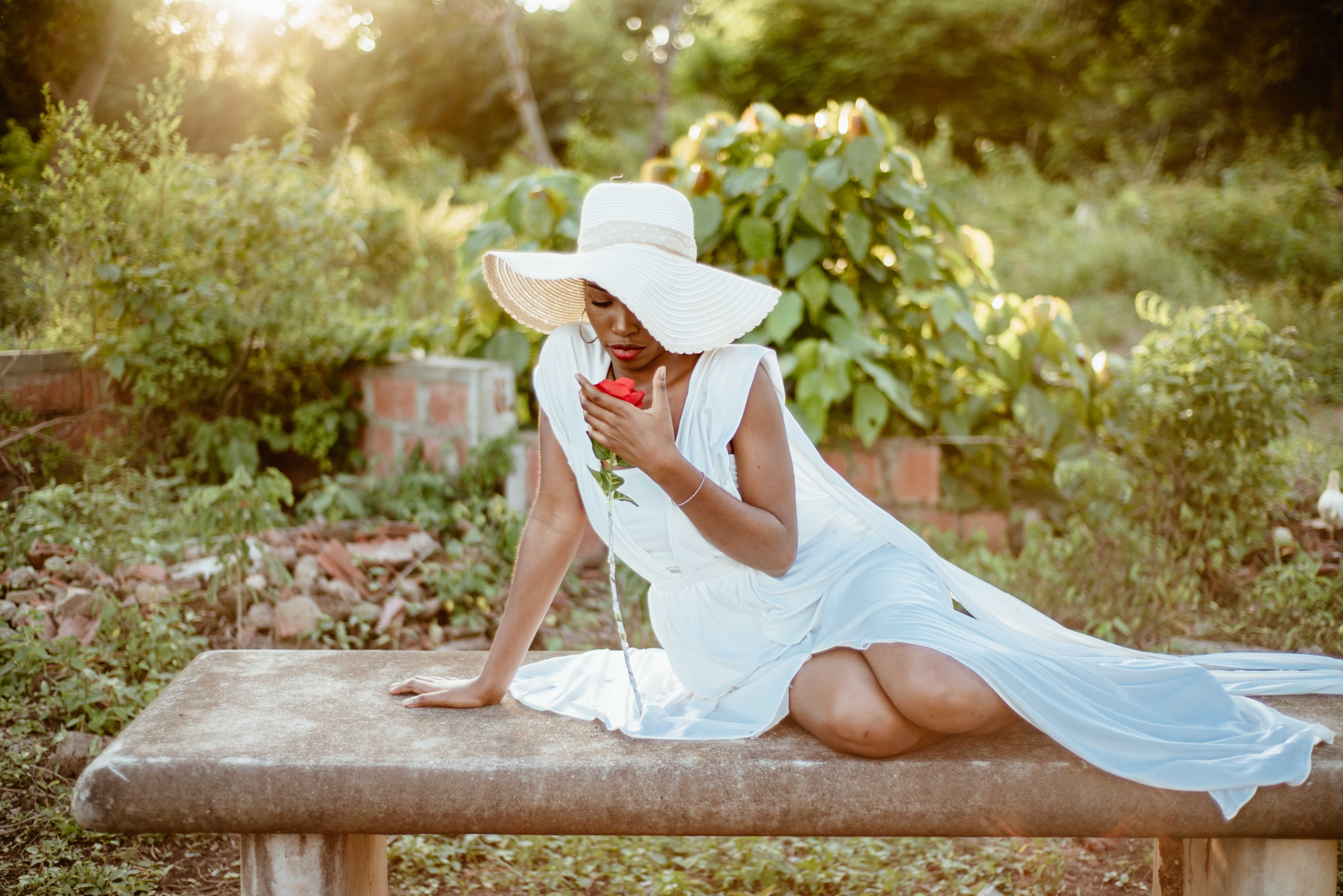 A woman in a white dress and hat sitting on a bench · Free Stock Photo