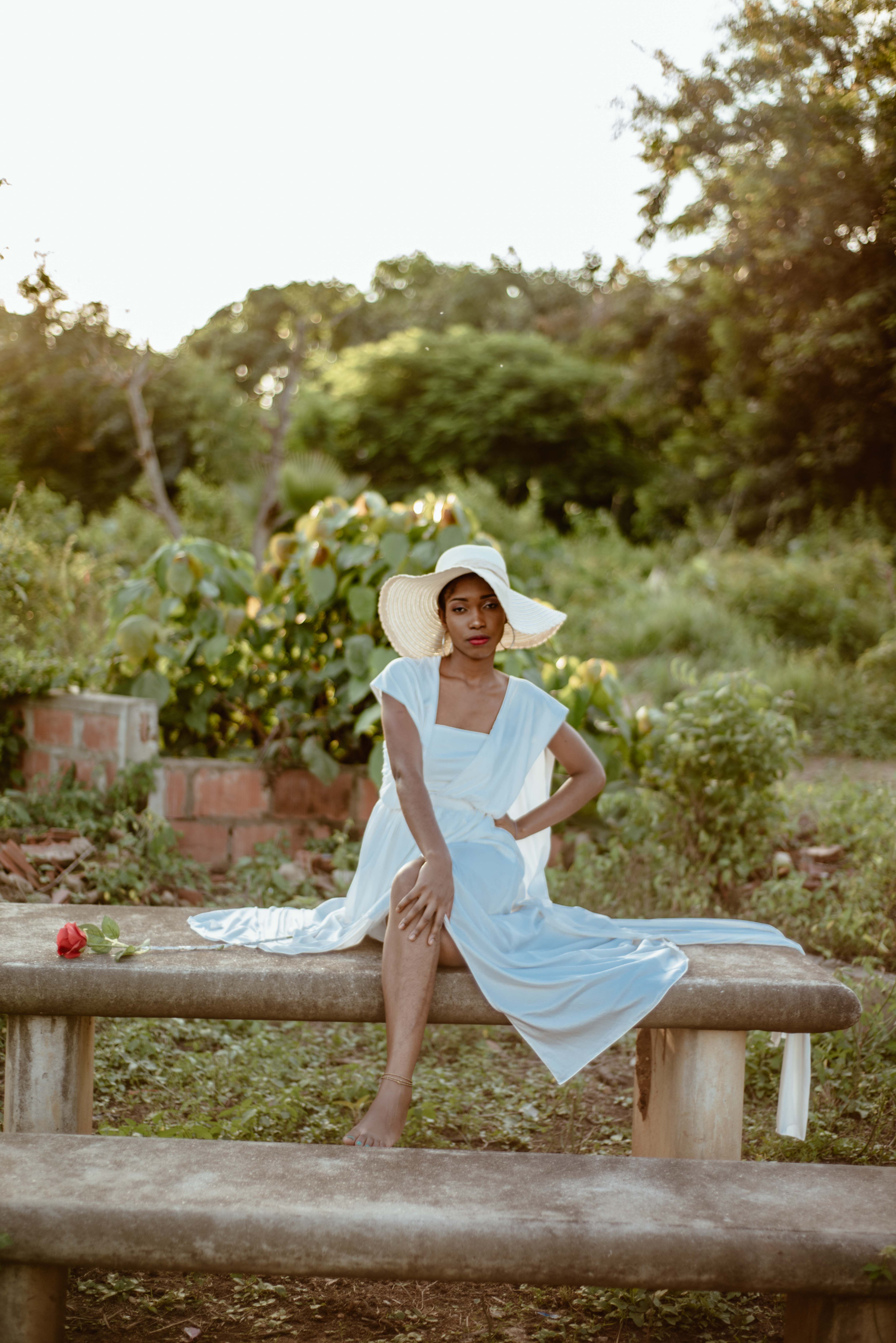 A woman in a white dress and hat sitting on a bench · Free Stock Photo