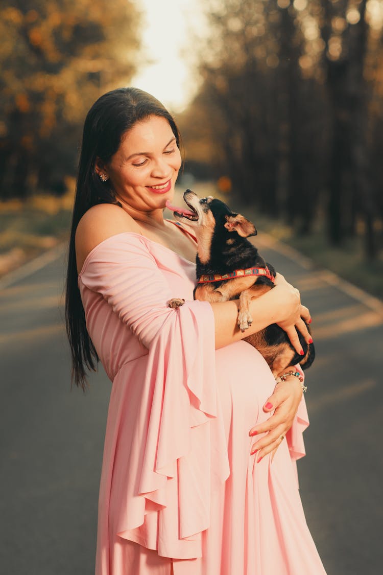 Pregnant Woman Posing Outside And Holding Her Dog 