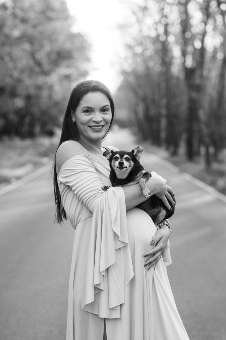 Pregnant Woman Posing Outside And Holding Her Dog 