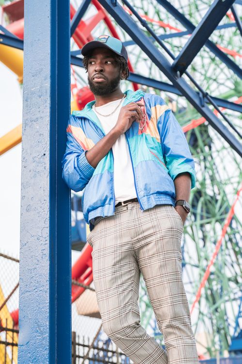 Free Fashionable man in a colorful jacket posing by a ferris wheel at Coney Island. Urban vibe. Stock Photo