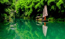 平静的河面上，倒映着一艘传统帆船，四周环绕着郁郁葱葱的绿叶