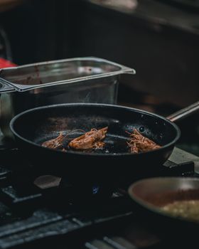 Sizzling prawns being cooked in a frying pan in a professional kitchen setting.