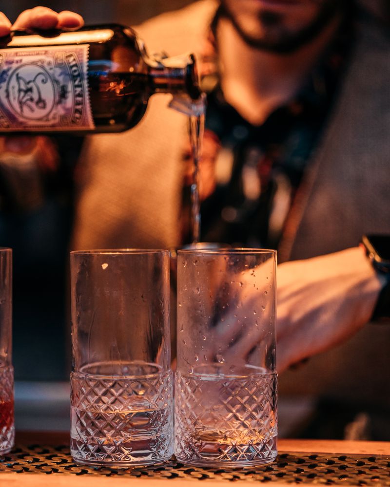 Bartender pouring drinks into glasses at a bar with warm lighting