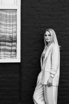 Black and white portrait of a stylish blonde woman in elegant attire against a brick wall.