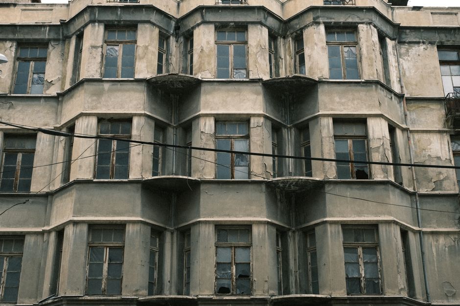 Weathered building facade with peeling render, cracked walls and water-damaged balconies showing salt-air deterioration
