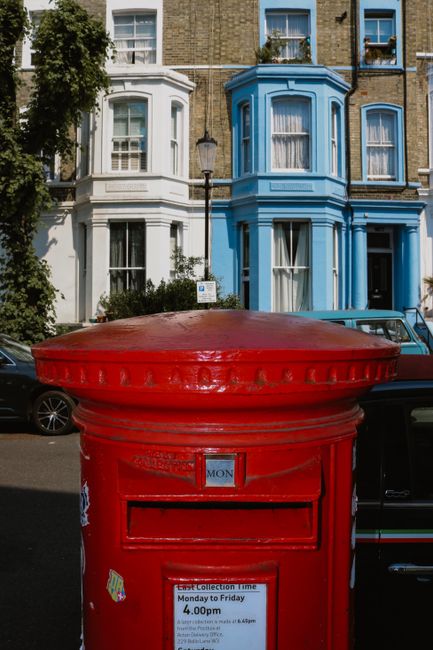 Iconic red mailbox in front of vibrant London townhouses on a sunny day.