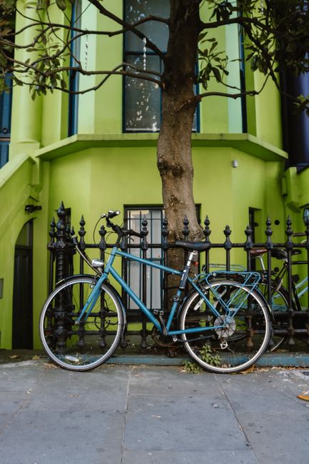 A blue bicycle rests against a decorative iron fence in front of a vibrant green building.