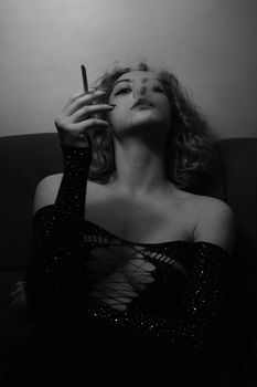 An artistic black and white portrait of a woman smoking in glamorous attire, exuding elegance and mystery.