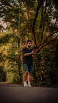 Young man with camera walking on a rural road amidst lush green forest and summer light.