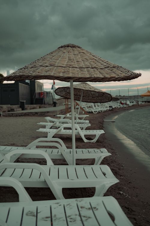 Free Empty sunbeds and thatched umbrellas on a calm beach under cloudy twilight skies. Stock Photo