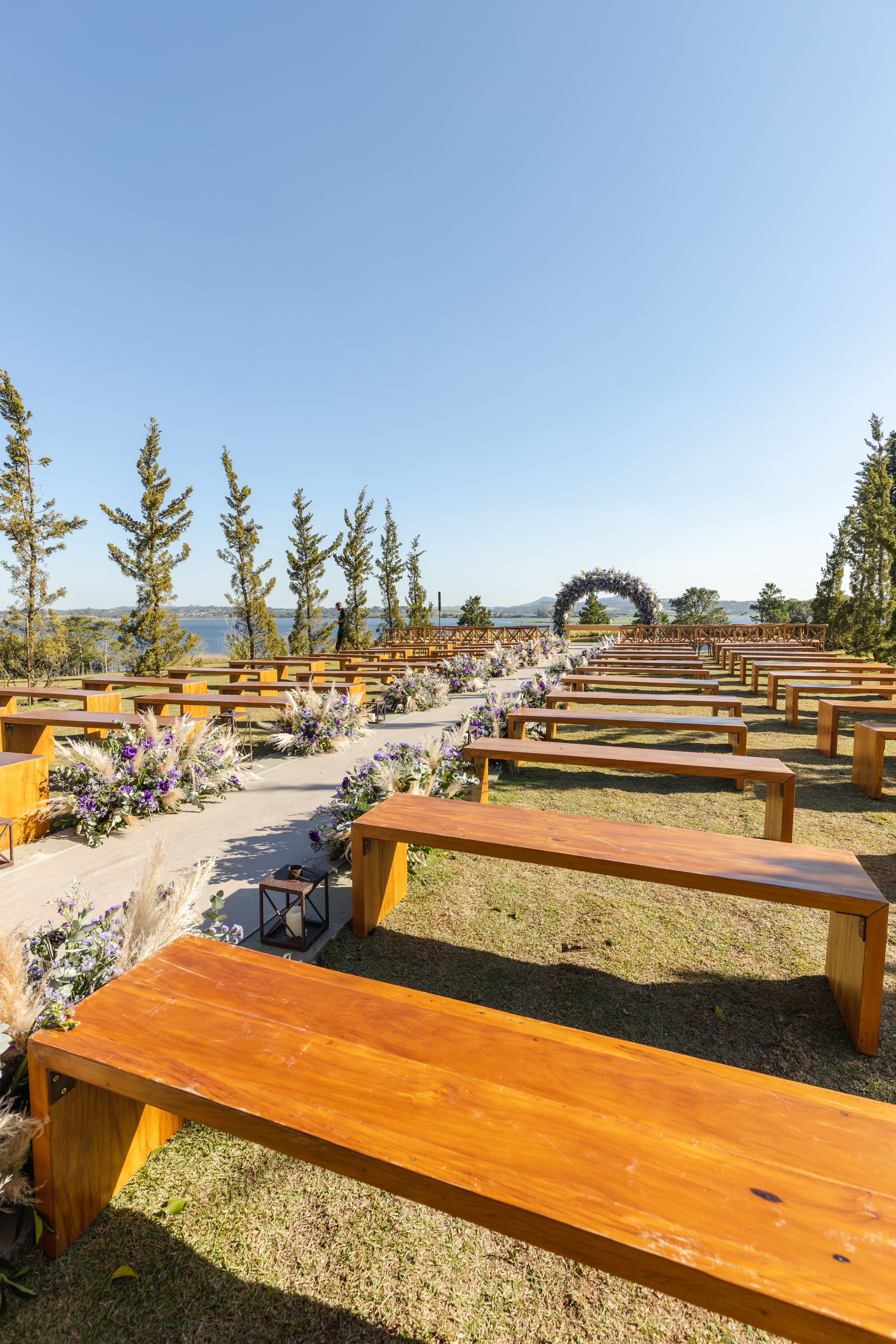 Fotomural Hermoso lugar de boda al aire libre con bancos de madera rústica y elegante decoración floral bajo un cielo claro.