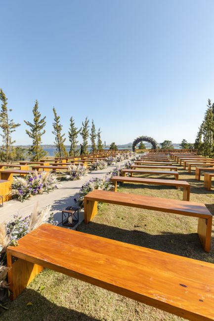Fotomural Hermoso lugar de boda al aire libre con bancos de madera rústica y elegante decoración floral bajo un cielo claro.