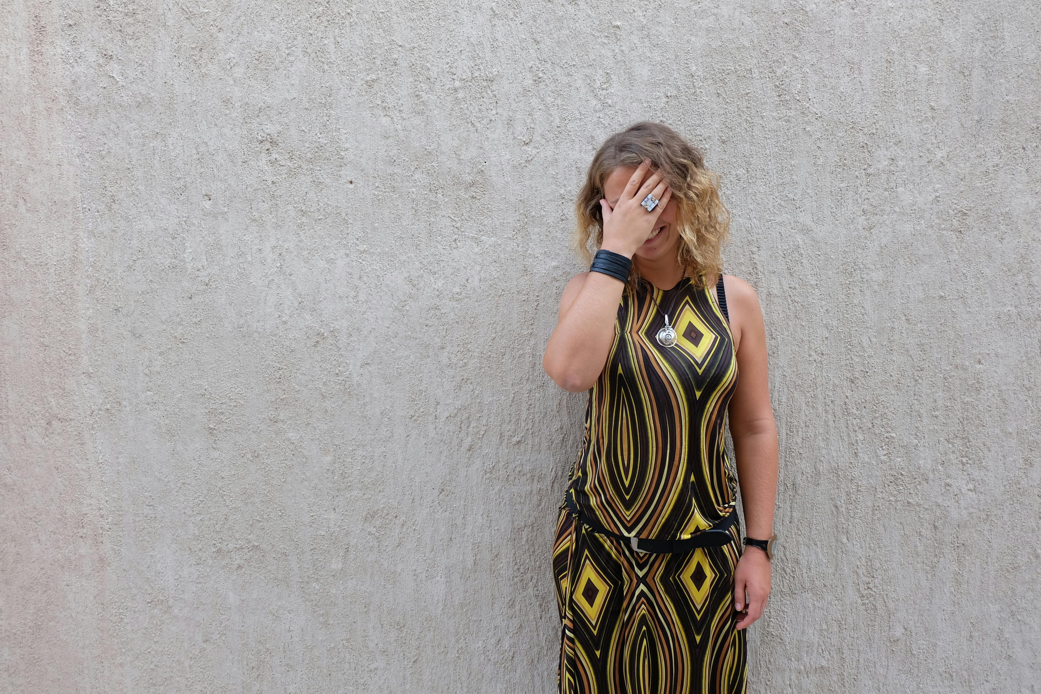 一位穿着几何连衣裙的时尚女性，靠在纹理墙壁上，用手遮住脸摆姿势