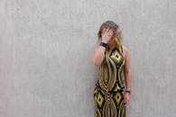 一位穿着几何连衣裙的时尚女性，靠在纹理墙壁上，用手遮住脸摆姿势