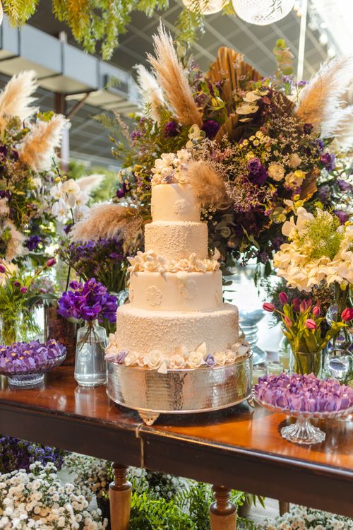 Free A beautiful tiered wedding cake surrounded by vibrant floral arrangements. Stock Photo