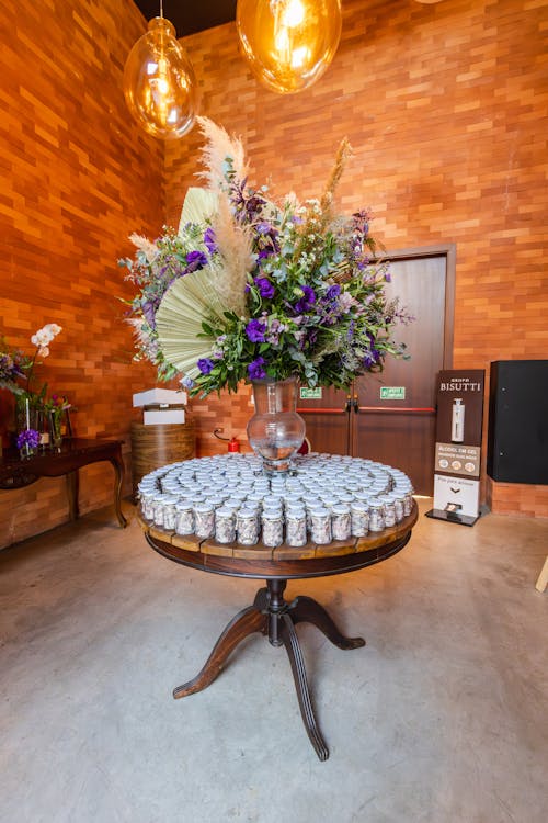 Elegant wedding favor display with jars of honey under a large floral arrangement on a round wooden table.