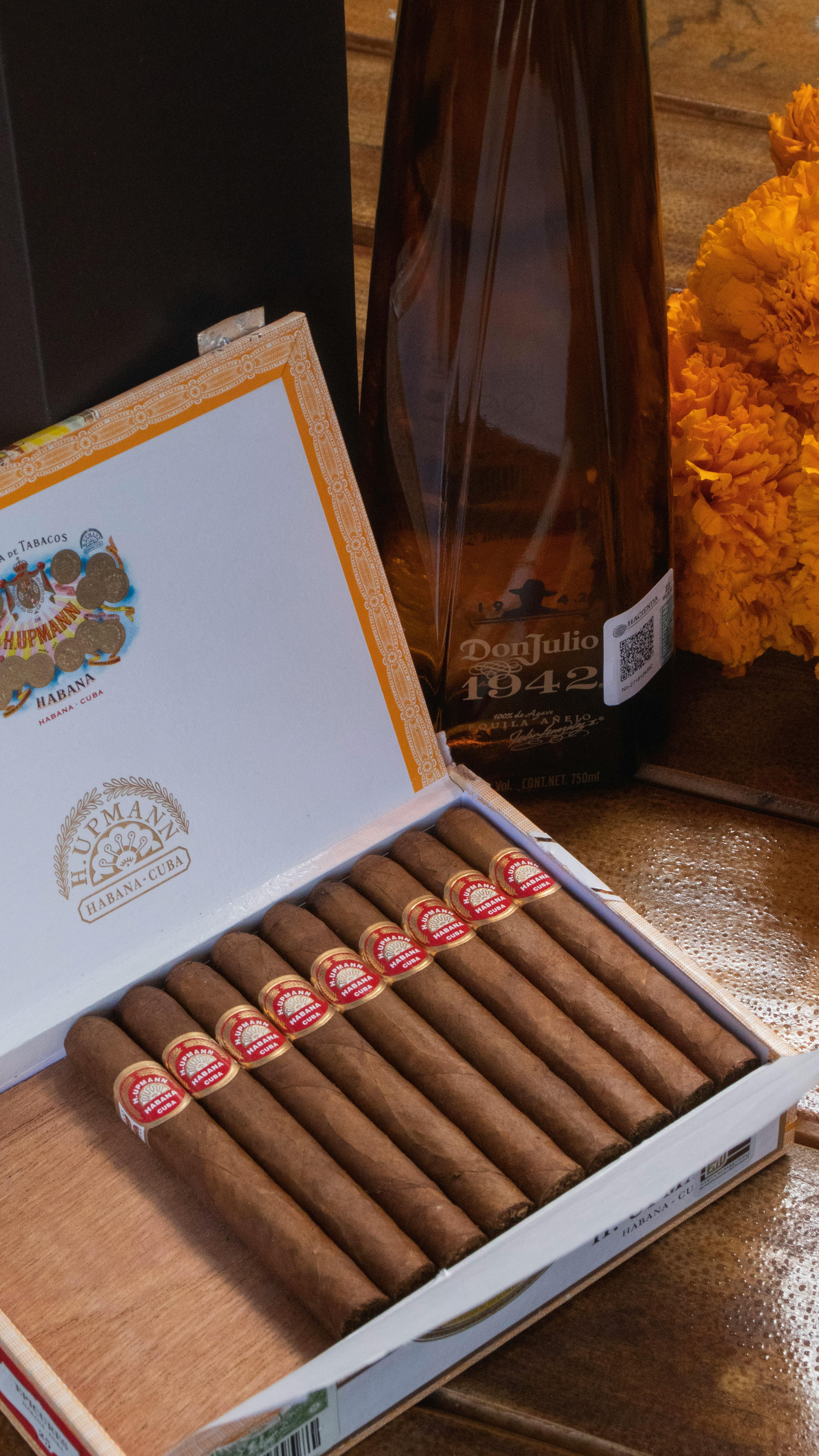 Box of Cuban cigars paired with Don Julio tequila bottle on a wooden table.